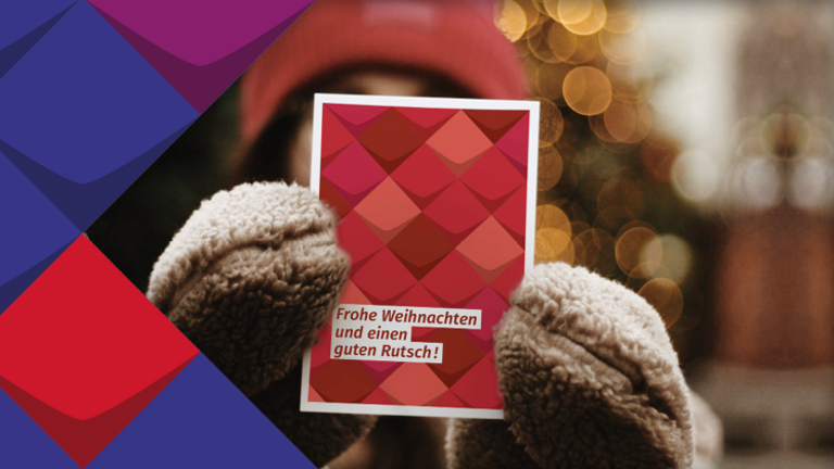 In Schmuckelemente der KSL.NRW (bunte Kacheln) ist ein Foto eingefasst: ein Mensch mit Mütze und Handschuhen bekleidet hält eine Karte so in die Kamera, dass sein Gesicht bedeckt ist. Auf der Karte steht frohe Weihnachten und einen guten Rutsch. 